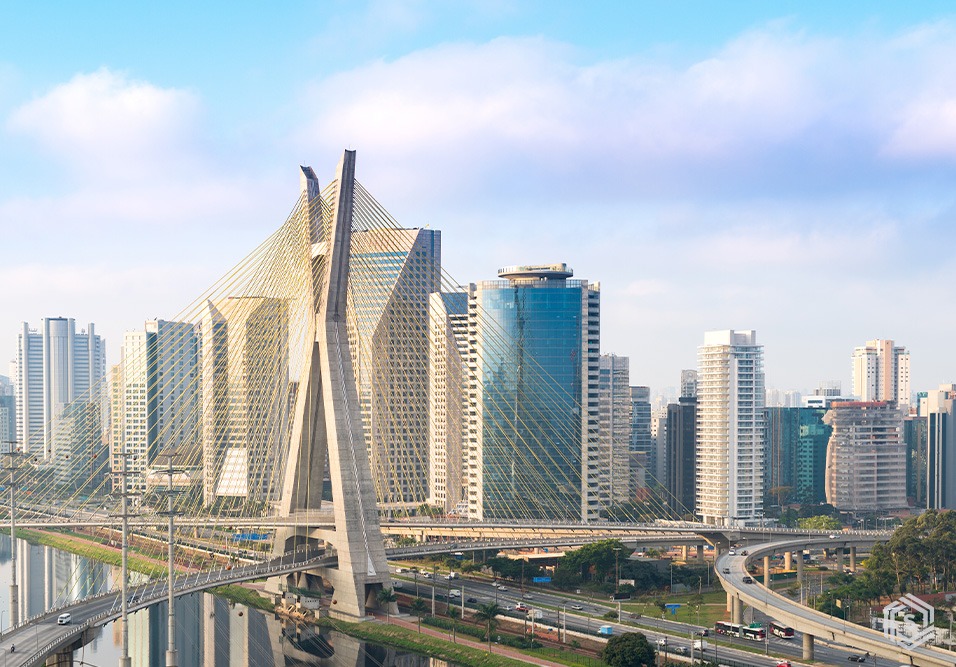 Imagem de moderno conjunto de arranha-céus em São Paulo, incluindo uma ponte estaiada e ruas movimentadas ao redor, representando arquitetura urbana