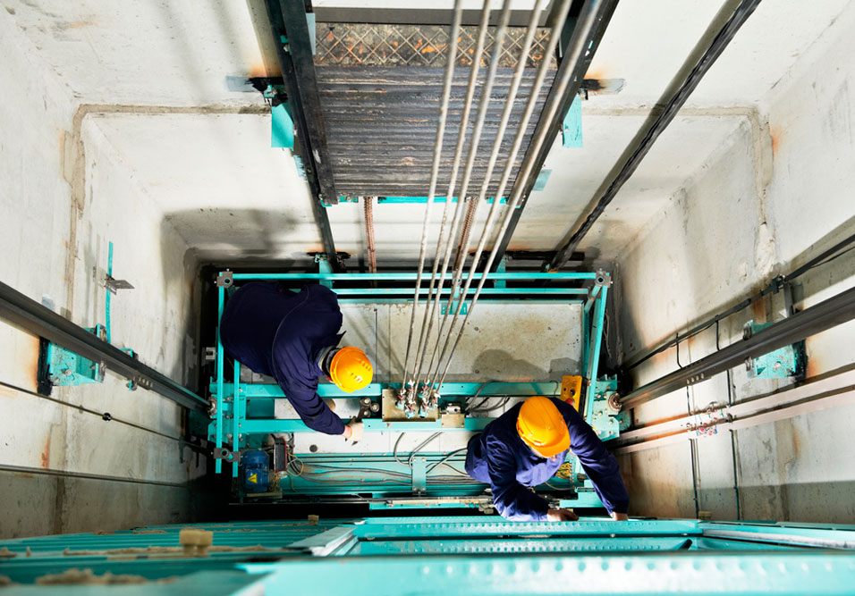Profissionais de manutenção em um fosso de elevador, trabalhando na instalação e inspeção de componentes do equipamento Profissionais de manutenção em um fosso de elevador, trabalhando na instalação e inspeção de componentes do equipamento