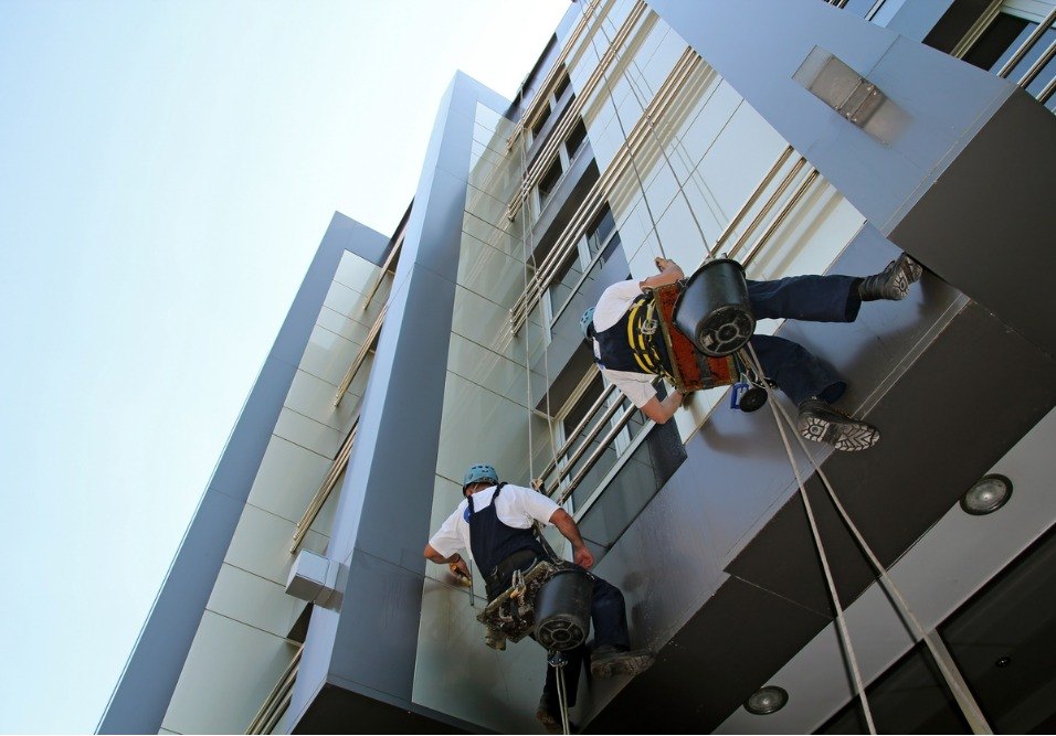 Profissionais realizando manutenção na fachada de edifício moderno, com equipamentos de segurança e ferramentas de trabalho.