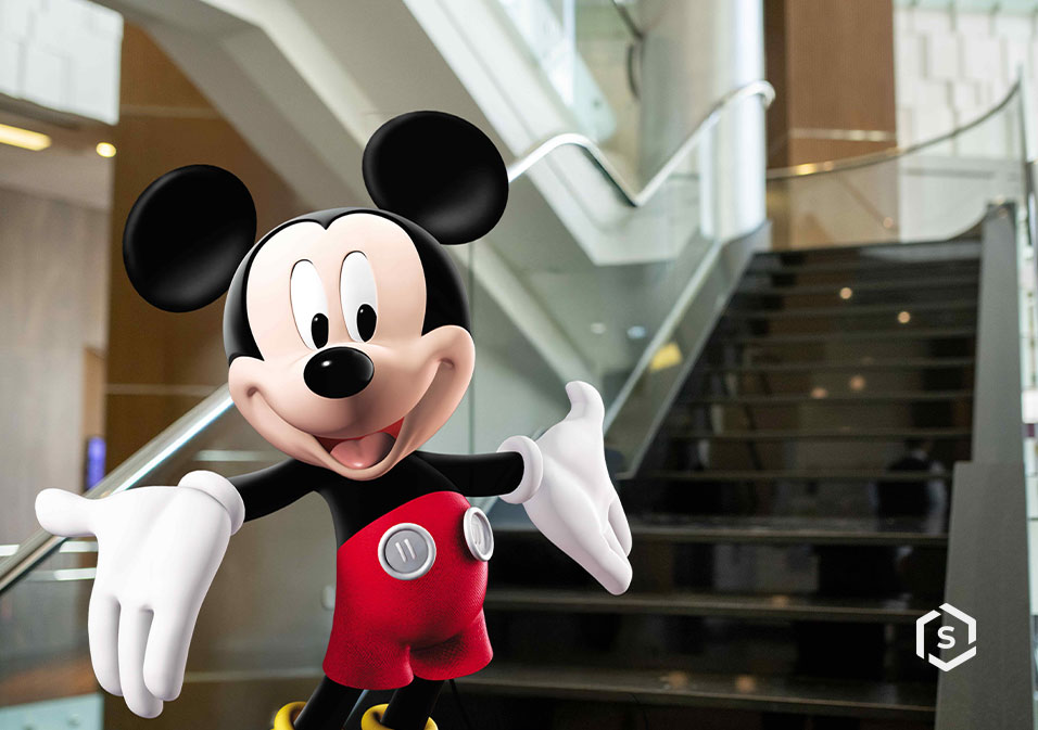 Imagem do Mickey Mouse, personagem icônico da Disney, com escada moderna e iluminação natural ao fundo em um prédio
