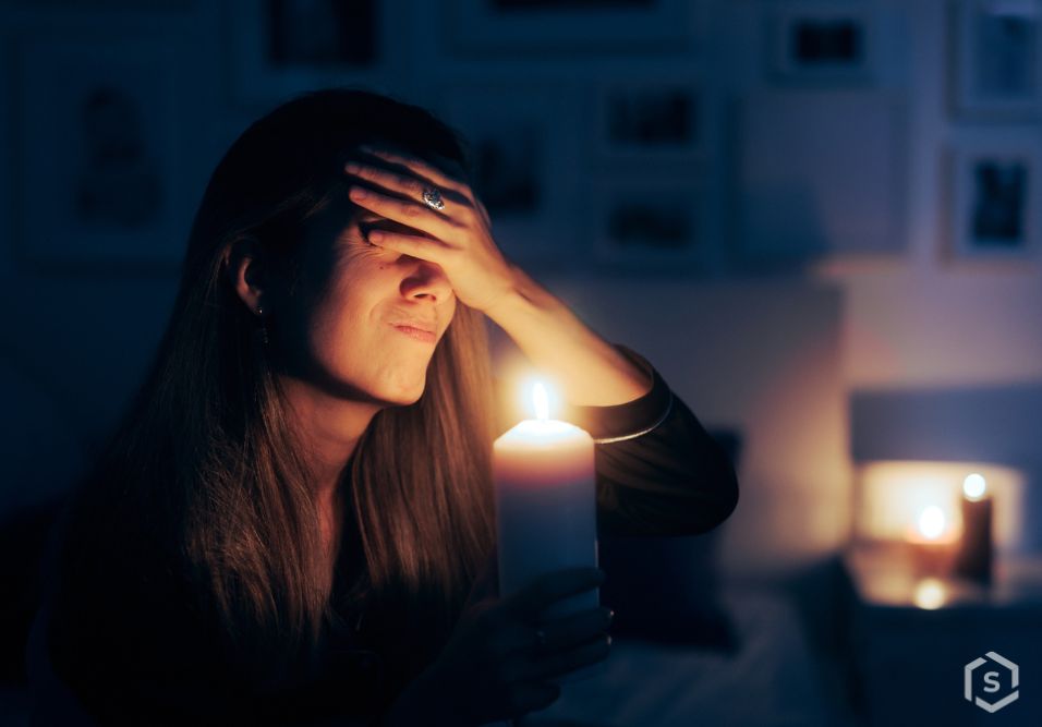 Mulher com expressão de preocupação/estresse segurando uma vela acesa em um ambiente escuro, transmitindo sensação de ansiedade ou problema emocional.