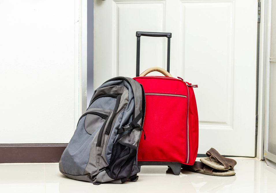 Conjunto de bagagem de viagem com mochila cinza, mala vermelha com rodinhas e um par de chinelos ao lado, pronto para uma viagem.