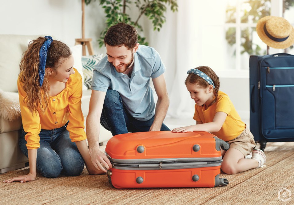 Família feliz preparando mala de viagem em casa, pronta para viajar. Crianças e pai rindo ao arrumar bagagem com mala laranja, cenário aconchegante.