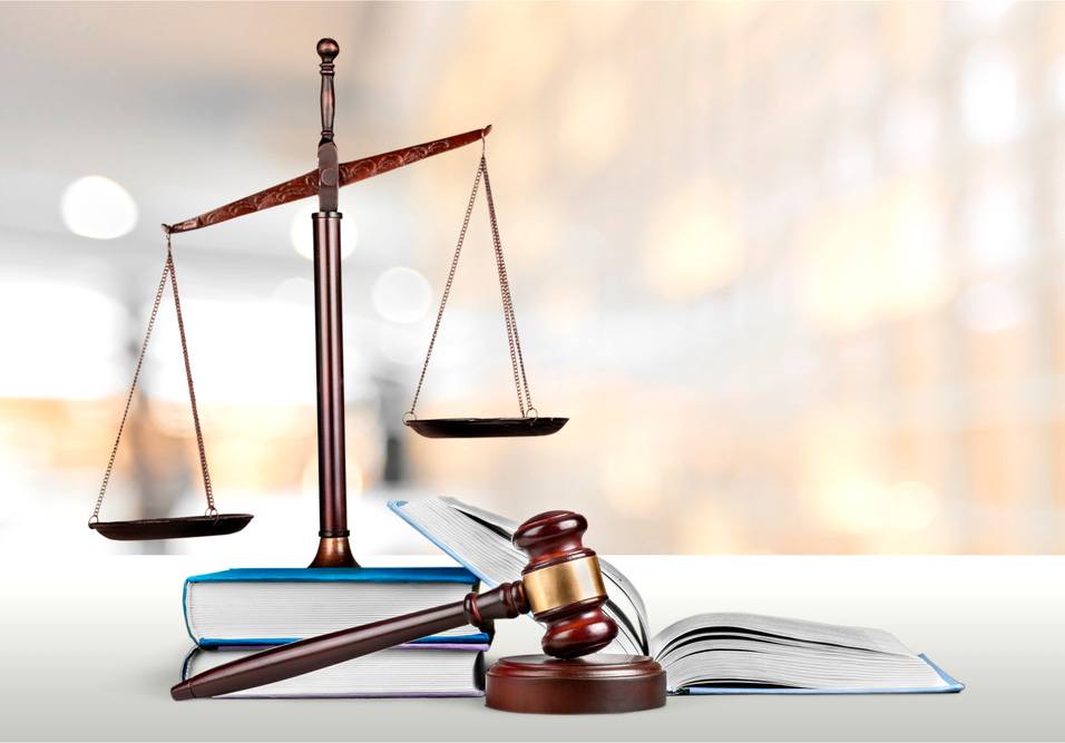 Imagem com balança de tribunal, martelo de juiz e livros de direito, simbolizando justiça e legislação.