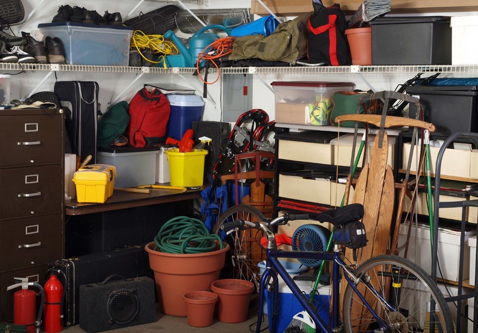 Imagem com objetos diversos, incluindo bicicleta, caixas, ferramentas e plantas entulhado em uma garagem de prédio.
