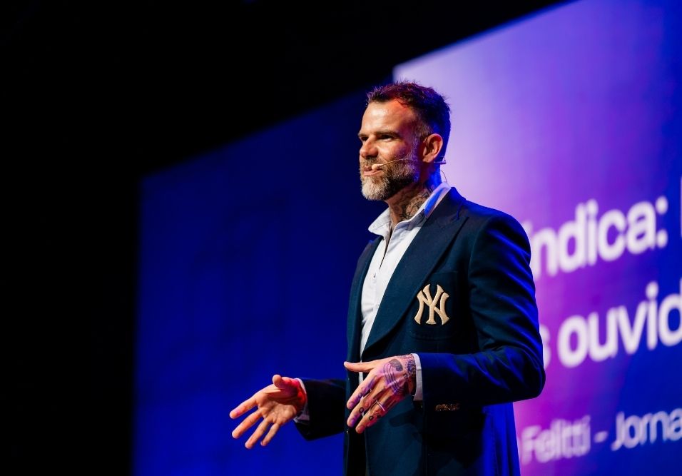 Jornalista Chico Felitti no palco do evento Superlógica Next 2026 em palestra sobre os podcasts O Síndico e A Síndica, vestindo blazer azul